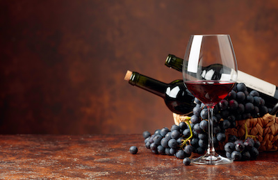Juicy blue grapes, glass and bottles of red wine on a brown background. Free space for your text.